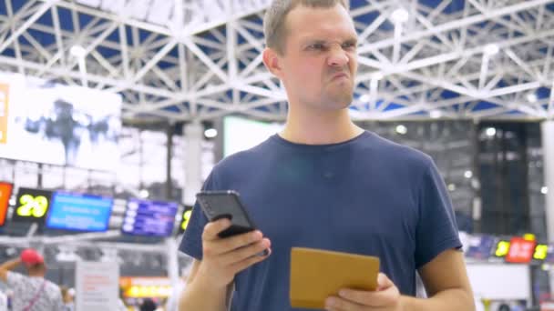 Schöner Mann am Flughafen im Wartezimmer. Mann sitzt mit Smartphone und hält Reisepass — Stockvideo