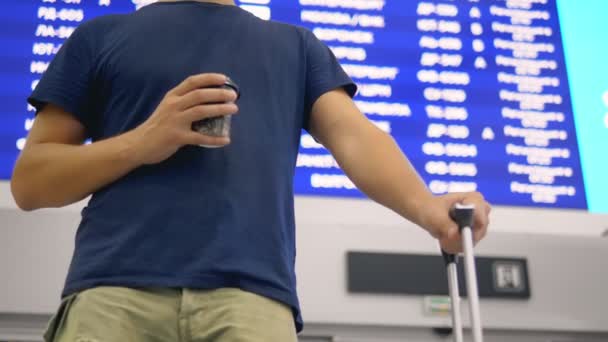 Conceito de viagem aérea. homem com uma mala e café fica na frente de uma placa de informações no aeroporto — Vídeo de Stock