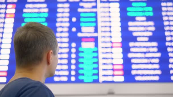 Концепция авиаперелетов. мужчина отступает и смотрит на расписание в аэропорту — стоковое видео