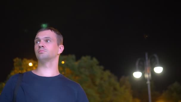 Λυπημένος ανήσυχος όμορφος άντρας στέκεται τη νύχτα στο δρόμο. με φόντο το νυχτερινό φωτισμό. Κοιτάζει γύρω και κοιτάζει το τηλέφωνό σας αναμένοντας κάτι — Αρχείο Βίντεο