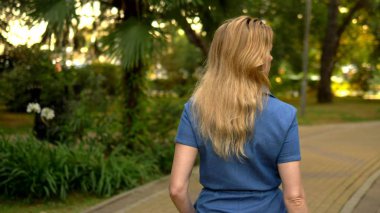arka görünüm. orta plan. denim tulum güzel genç kadın sarışın yaz şehir parkı ile yürür
