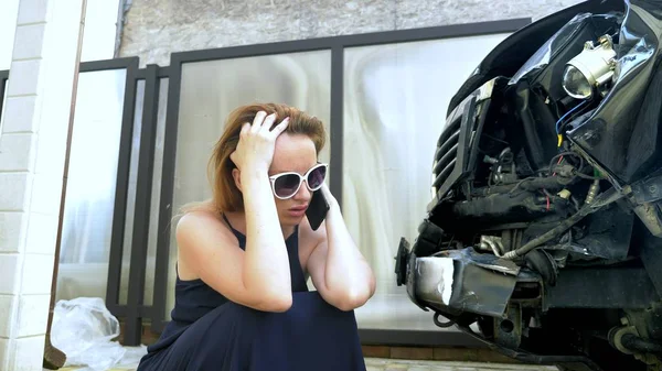 Car accident concept. woman in a state of shock talking on the phone after a car accident, standing by a car with a broken bumper — Stock Photo, Image