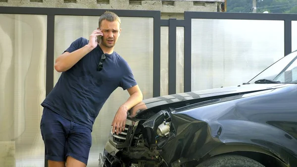 Car accident concept. man in a state of shock talking on the phone after a car accident, standing by a car with a broken bumper — Stock Photo, Image