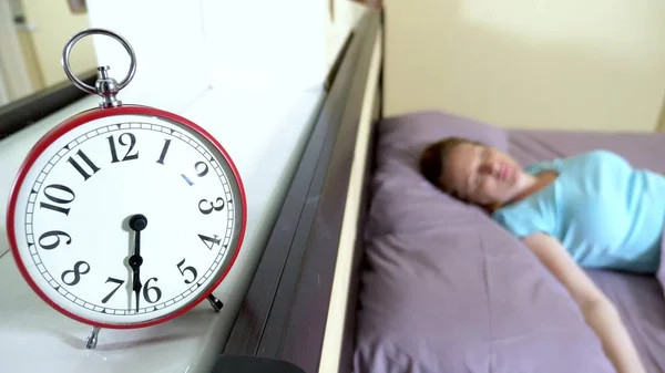 Red alarm clock close-up, on a blurred background, the girl is angry that the alarm clock has rung