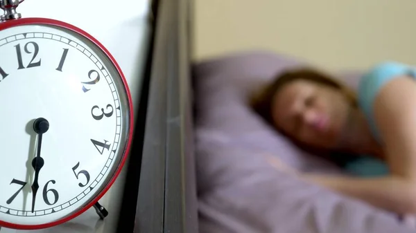 Red alarm clock close-up, on a blurred background, the girl is angry that the alarm clock has rung — Stock Photo, Image