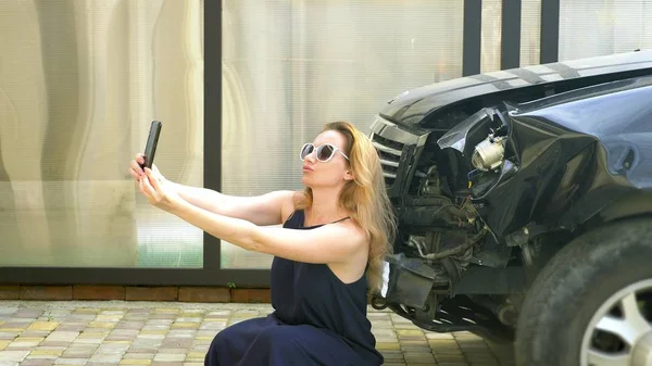 Wanita pirang memotret selfie di smartphone-nya setelah kecelakaan bumper rusak. aneh, petualangan orang-orang aneh — Stok Foto