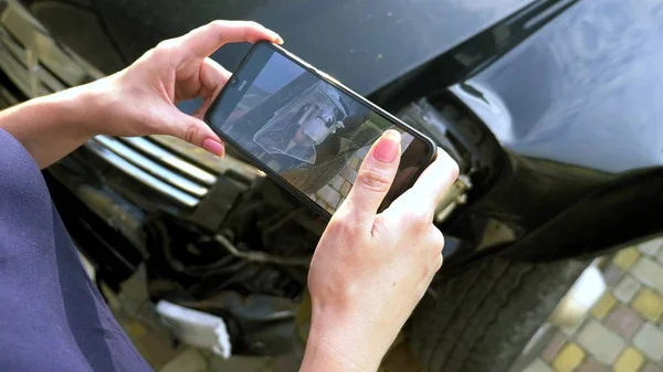 Uma mulher tira uma foto em seu smartphone após o acidente de um pára-choques carro quebrado — Fotografia de Stock