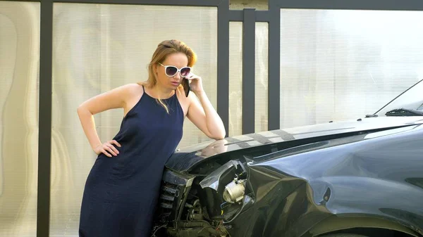 Автомобильная авария. женщина в состоянии шока разговаривает по телефону после автомобильной аварии, стоит у машины со сломанным бампером — стоковое фото