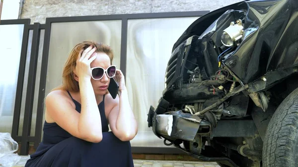 Conceito de acidente de carro. mulher em estado de choque falando ao telefone após um acidente de carro, em pé junto a um carro com um pára-choques quebrado — Fotografia de Stock