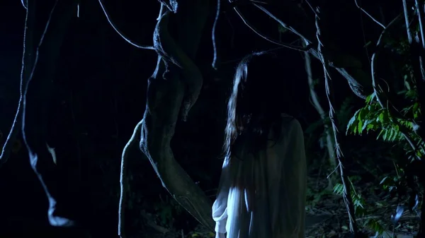 할로윈. 긴 검은 얼굴 머리를 가진 유령 소녀는 번개플래시의 두꺼운 무서운 숲에 서. — 스톡 사진