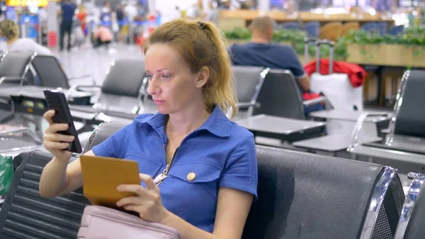 Frau am Flughafen im Wartezimmer. Mädchen sitzt mit Smartphone und hält Reisepass mit Gepäck. — Stockfoto