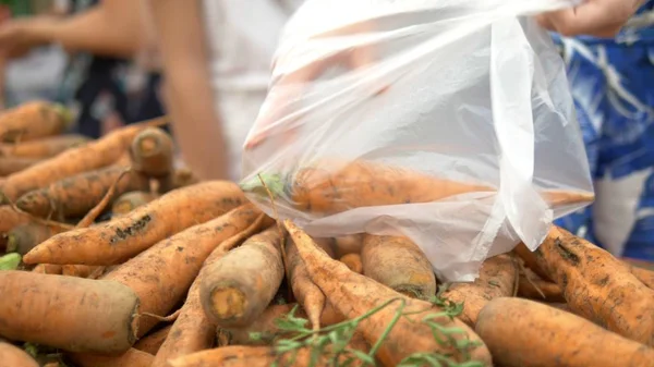 Social market concept, cheap products. women picks up dirty carrots on the counter in the store in a plastic bag — Stock Photo, Image