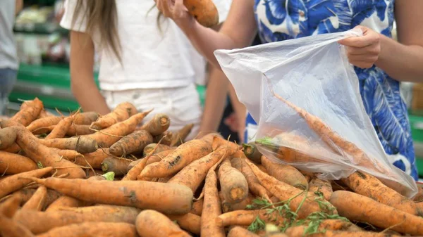 Social market concept, cheap products. women picks up dirty carrots on the counter in the store in a plastic bag — Stock Photo, Image