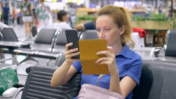 Frau am Flughafen im Wartezimmer. Mädchen sitzt mit Smartphone und hält Reisepass mit Gepäck. — Stockfoto