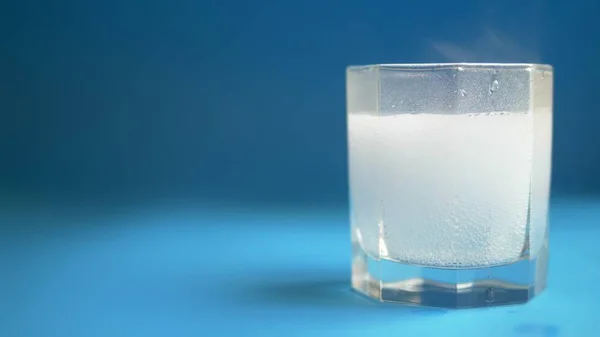 Close-up. pílula dissolver em água com bolhas no fundo azul. espaço de cópia — Fotografia de Stock