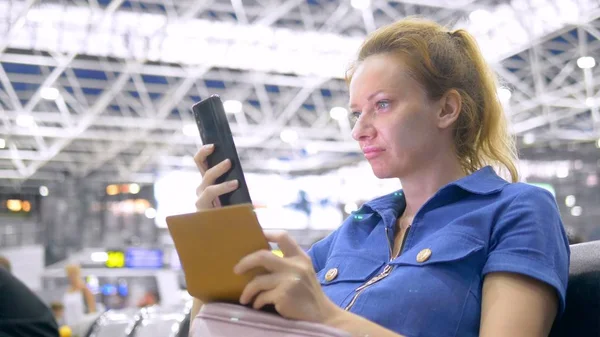 Frau am Flughafen im Wartezimmer. Mädchen sitzt mit Smartphone und hält Reisepass mit Gepäck. — Stockfoto