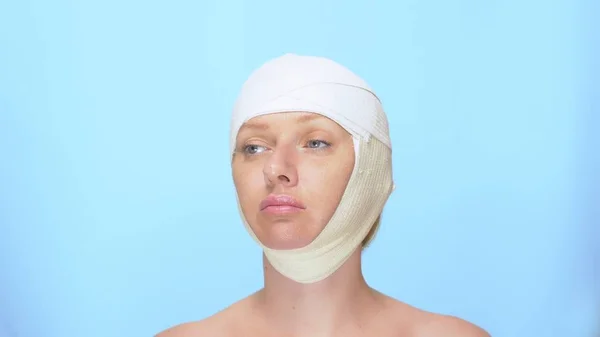 Das Konzept der plastischen Chirurgie. Facelifting. Porträt einer Frau mit einem Verband auf dem Kopf, auf blauem Hintergrund. — Stockfoto