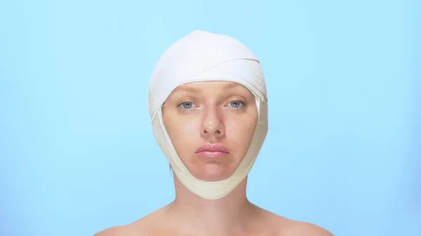 The concept of plastic surgery. face lift. Portrait of a woman with a bandage on his head, on a blue background. — Stock Photo, Image