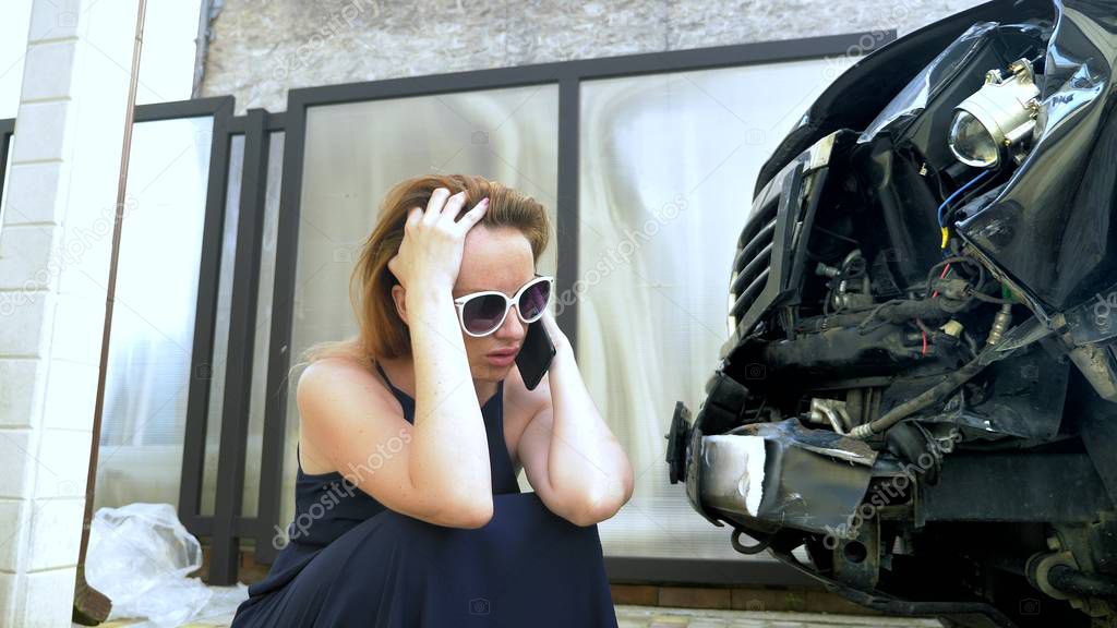 car accident concept. woman in a state of shock talking on the phone after a car accident, standing by a car with a broken bumper