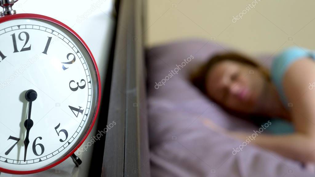 Red alarm clock close-up, on a blurred background, the girl is angry that the alarm clock has rung