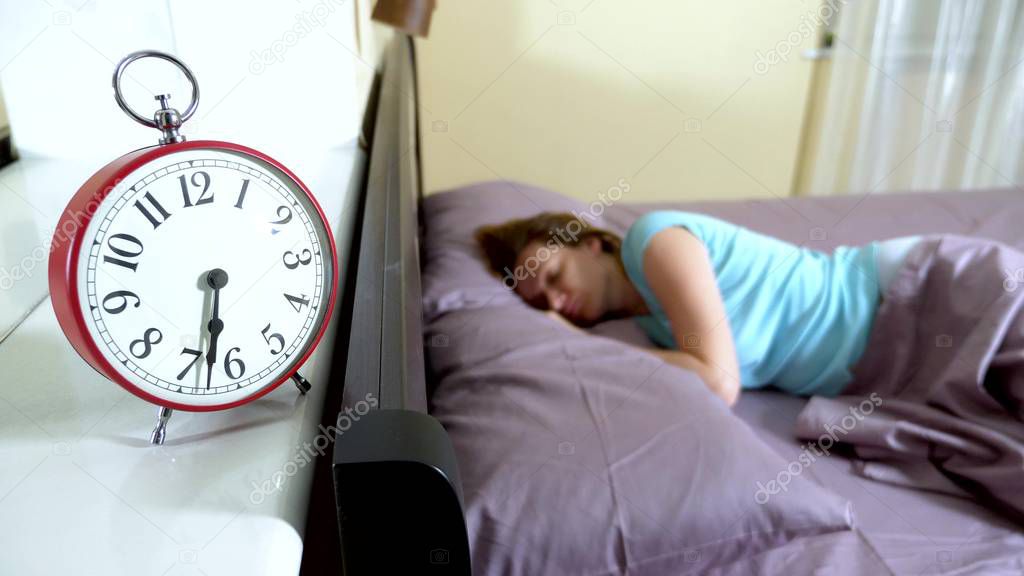 Red alarm clock close-up, on a blurred background, the girl is angry that the alarm clock has rung