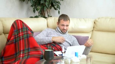 bir süveter kanepede oturan soğuk bir adam ve bir ekose video bağlantısı üzerinden bir dizüstü bilgisayar üzerinde Doktor çağırma.