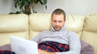 bir süveter kanepede oturan soğuk bir adam ve bir ekose video bağlantısı üzerinden bir dizüstü bilgisayar üzerinde Doktor çağırma.