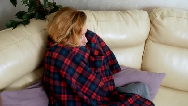 Femme dans une maison sur le canapé couché sous un plaid à la maison souffrant de froid et de fièvre. Le concept de virus du rhume et de la grippe — Video