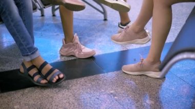 bekliyor, bacaklar yakın. Bir grup insan bekleme odasında oturuyor..