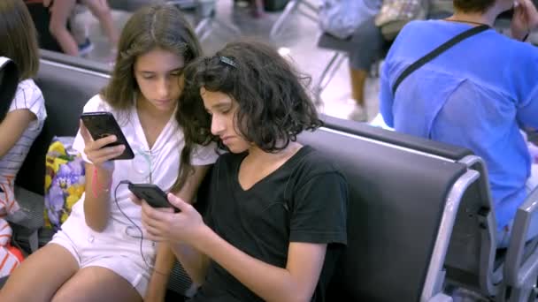 As crianças na área de espera do aeroporto usam um smartphone. conceito de viagem — Vídeo de Stock