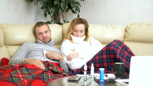 Concept of cold and flu virus, epidemic. husband and wife with fever lie on the living room sofa in sweaters and under blankets — Stock Video