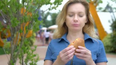 Genç kadın yürüyüş insanların arka planda parkta oturan iştah açıcı bir hotdog yeme, arka plan bulanık.