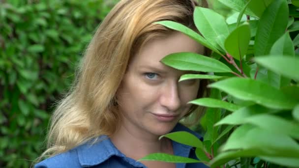 Close-up. Vrouw verstopt in het midden van een heggen doolhof op een zonnige zomerdag. Ze kijkt naar de camera. — Stockvideo