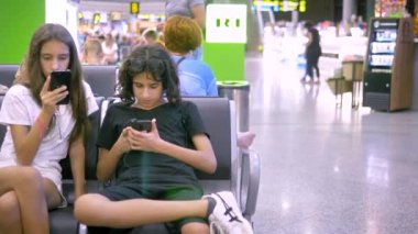 Havaalanında bekleyen çocuklar bir akıllı telefon kullanır. seyahat konsepti