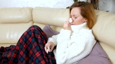 Deliksiz bir burun ile güzel bir kadın evde bir burun spreyi kullanır, oturma odasında kanepede oturan, bir kazak ve bir battaniye altında