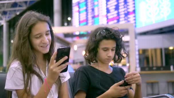 Los niños en la sala de espera del aeropuerto utilizan un teléfono inteligente. concepto de viaje — Vídeo de stock