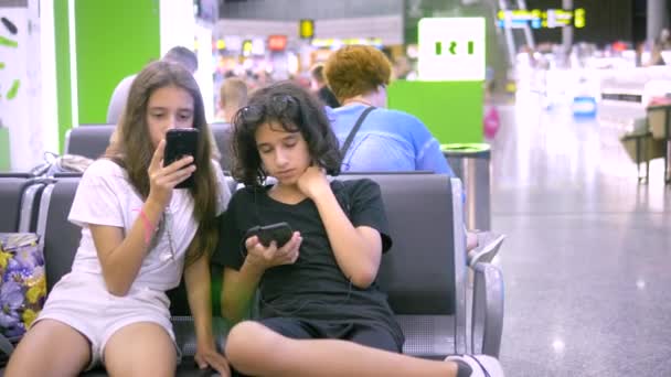 Les enfants dans la salle d'attente de l'aéroport utilisent un smartphone. concept de voyage — Video