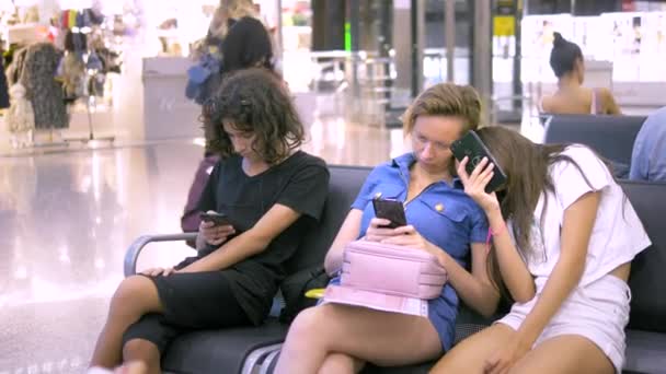 Una mujer y dos niños en el área de espera del aeropuerto utilizan un teléfono inteligente. concepto de viaje — Vídeos de Stock