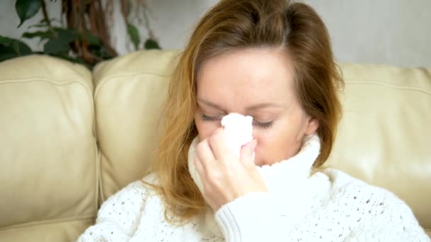 Schöne Frau mit laufender Nase benutzt zu Hause ein Nasenspray, sitzt auf dem Sofa im Wohnzimmer, im Pullover und unter einer Decke — Stockvideo
