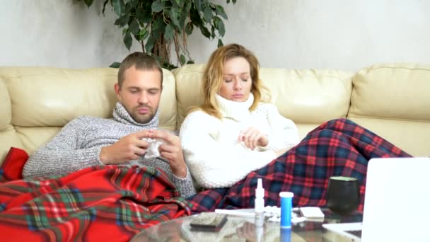 Concepto de virus del resfriado y la gripe, epidemia. marido y mujer con fiebre se encuentran en el sofá de la sala de estar en suéteres y debajo de las mantas — Vídeos de Stock