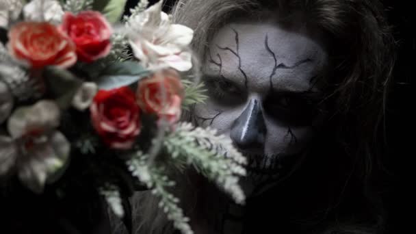 Concept, beautiful makeup for halloween. Portrait of a young sexy girl with make-up of a skull and a bouquet of flowers. — Stock Video