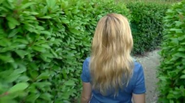 Kısa denim tulum bir kadın güneşli bir yaz gününde bir hedge labirent yürürken. arka görünüm