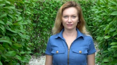 Güneşli bir yaz gününde bir hedge labirent ortasında duran kısa denim tulum bir kadın. Kameraya bakıyor.