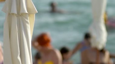 Bulanık arka plan. Sahilde plaj sandalyeleri ve şemsiyeler, tanınmayan insanlar istirahat