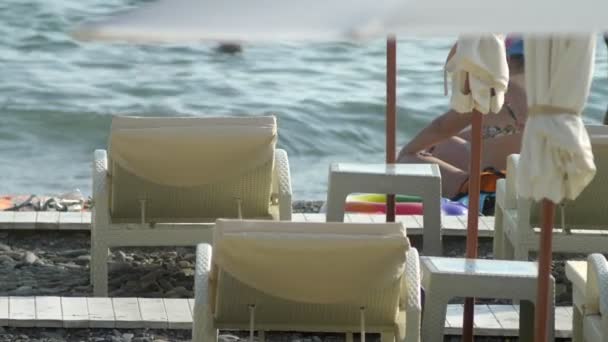 Размытое прошлое. пляжные стулья и зонтики на пляже, неузнаваемые люди отдыхают — стоковое видео