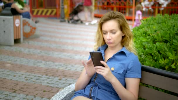 Νεαρή γυναίκα χρησιμοποιεί smartphone στο πάρκο ψυχαγωγίας. Ανεξάρτητη ιδέα, λειτουργεί απομακρυσμένα — Αρχείο Βίντεο
