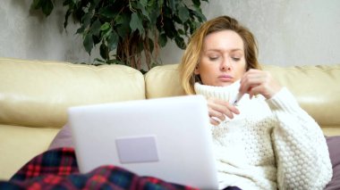 bir kazak ve bir dizüstü bilgisayar üzerinden video bağlantısı ile Doktor çağıran bir ekose kanepede oturan soğuk ile sarışın kadın. Orta çekim