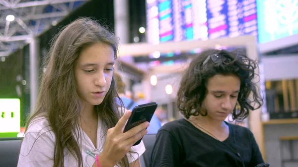 Los niños en la sala de espera del aeropuerto utilizan un teléfono inteligente. concepto de viaje —  Fotos de Stock
