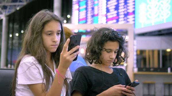 As crianças na área de espera do aeroporto usam um smartphone. conceito de viagem — Fotografia de Stock