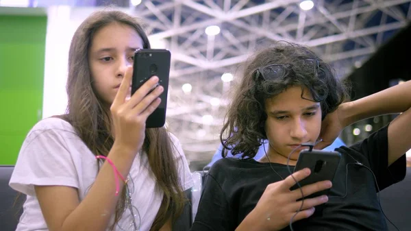 Los niños en la sala de espera del aeropuerto utilizan un teléfono inteligente. concepto de viaje — Foto de Stock